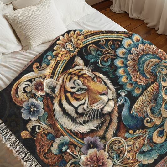 A woven blanket featuring a baroque-inspired design with a tiger and peacock, surrounded by ornate floral and golden scrollwork, draped over a bed.